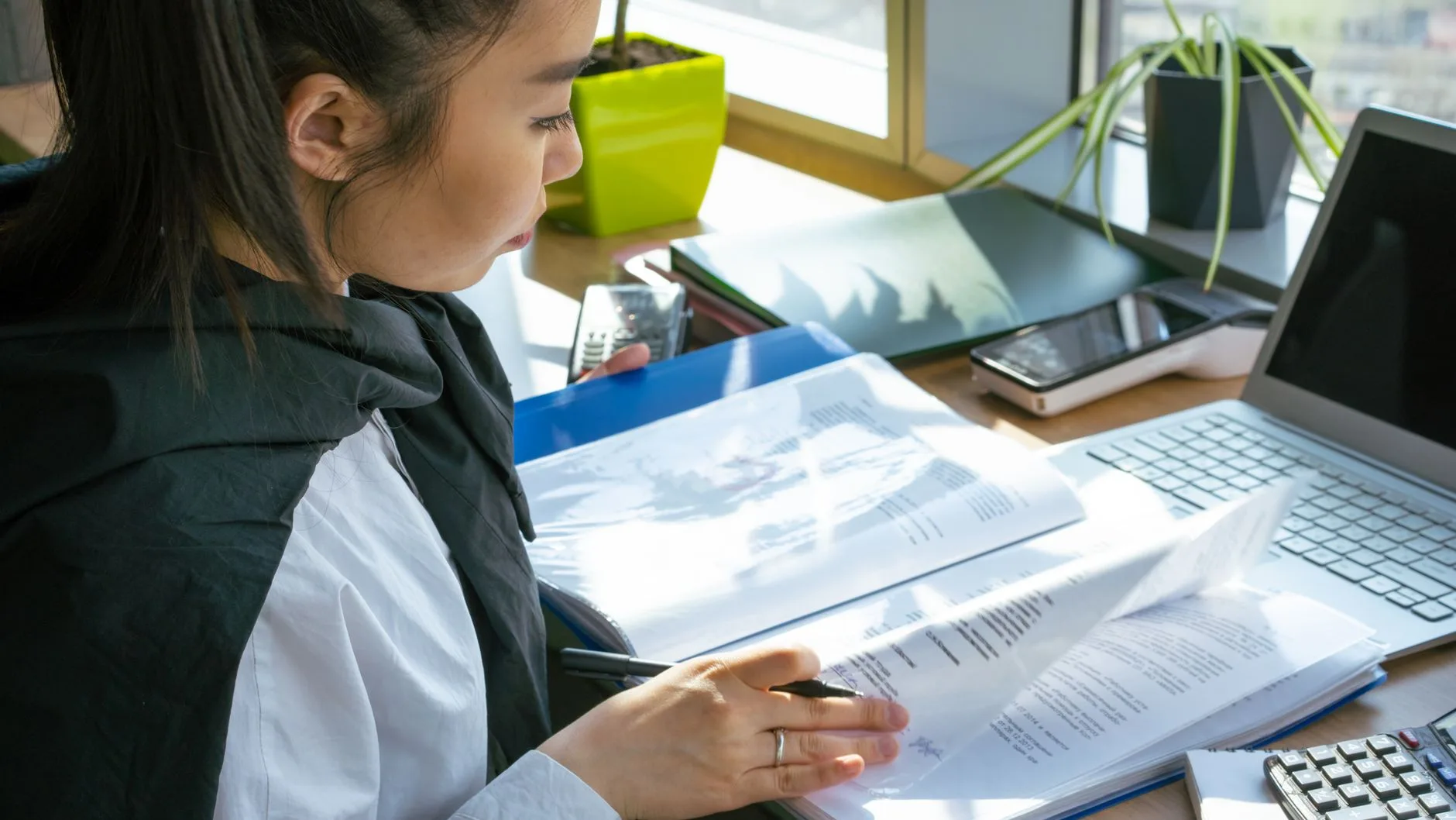 Focused woman reviewing documents at a desk with a laptop and stationery.